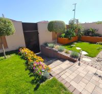 The garden of a family house in Martin nad Žitavou with flower beds and a paved walkway.