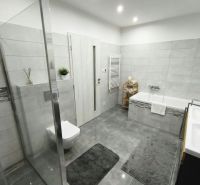 A bathroom in a family house with a bathtub, a shower corner, and tiles in a gray design.