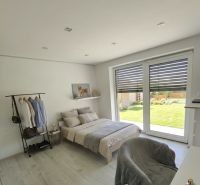 A bright bedroom in a family house with wood-decor flooring and large windows.