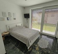 A bedroom in a family house with a bed and a television, marble floor, large window.