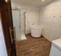 A bathroom with a bathtub and a shower, a floor with a wooden decor in a family house.