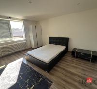 A bedroom with light from a window, a bed, a wardrobe, and a floor with a wooden decor.