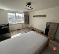 A bedroom in a 4-room apartment with a wooden decor floor, simple furniture, and a large window.