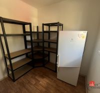 A room in a 4-room apartment with shelves, a refrigerator, and a wooden decor floor.