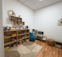 Children's corner in the office with shelves full of toys, floor with wooden decor.