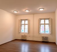A room with two windows, white walls, and a wooden-patterned floor. Offices.
