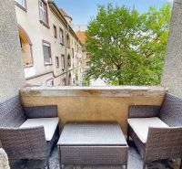 The balcony of a 3-room apartment in Nitra with rattan furniture and a view of a tree.