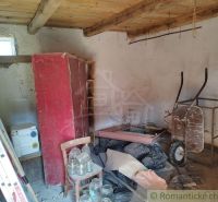 The interior of a cottage with a red wardrobe, a wheelbarrow, and wooden beams on the ceiling.