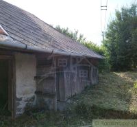 An old cottage in Hrušov with wooden walls and a shingle roof, surrounded by lush vegetation.