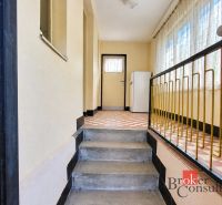 Hallway in a family house with stairs, railing, and tiles.