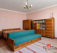 A room in a family house with retro furniture, patterned wallpaper, and a sofa.