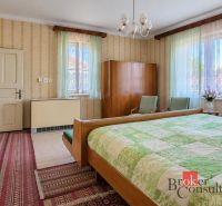 A bedroom in a family house with vintage furniture, wallpaper, and green curtains.