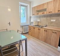 A kitchen in a 2-room apartment with a wood-patterned floor, a glass table, white walls.
