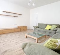 Living room of a two-room apartment with a couch, table, and shelves, floor with wooden decor.