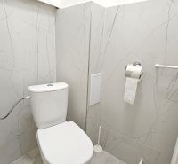 A bathroom in a 2-room apartment with marble tiles and a toilet.