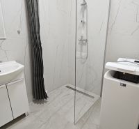 Bathroom with a shower in a 2-room apartment; sink, washing machine, light tiles.