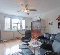 Living room in a 3-room apartment with a wooden decor floor, black sofa, and armchairs.