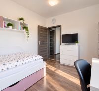 A room in a family house with a bed, furniture, a television, and a floor with a wooden decor.