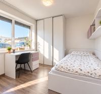 A room with white furniture, a table by the window, plants, and a wooden decor floor.