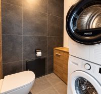 A bathroom in a family house with a washing machine and dryer, gray and wooden tiles.