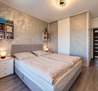 Bedroom in a family house with wood-patterned flooring, light-colored walls, and a bed.