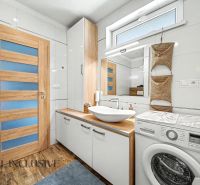 Bathroom in a family house with a washing machine, sink, and floor with wooden decor.