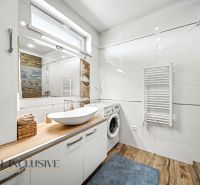 A bathroom in a family house with a sink, a washing machine, and a floor with a wooden decor.