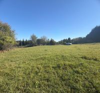 Residential plots in Podvysoká, a green meadow with a car in the background, surrounded by trees.