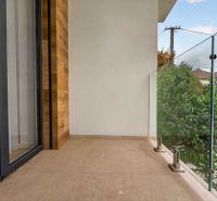 A balcony in a family house with glass railings and a view of greenery.