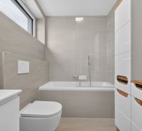 A bathroom with a bathtub and storage space in a family house, with a large window.