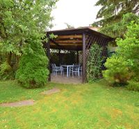 A garden gazebo surrounded by greenery and trees, with outdoor seating.
