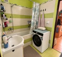 A bathroom with a bathtub, a washing machine, and green tiles in a 2-room apartment.