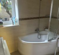 Bathroom with a bathtub, shower screen, and window in a 3-room apartment.