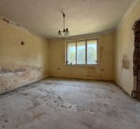 A room in a family house with a window, peeling plaster, and an unfinished floor.