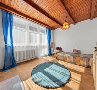 A room in a family house with a wooden decor floor, blue curtains, and a large window.