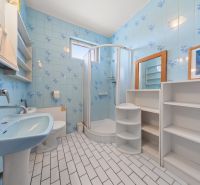 A bathroom with blue tiles, a shower enclosure, and white furniture in a family house.
