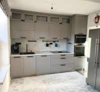 A kitchen in a family house with gray cabinets and a patterned rug on a wood-decorated floor.