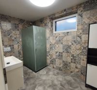 A bathroom in a family house with patterned tiles and a shower corner.