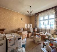 A room in a family house with cardboard boxes, wallpaper walls, wood-decorated floor, curtains.
