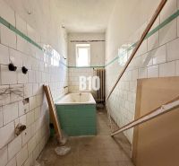A family house bathroom with worn-out tiles and a bathtub awaiting renovation.