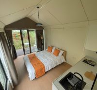 A cottage with a wooden floor decor, a simple bed, a small kitchenette, and a balcony.
