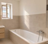 A bathroom in a family house with a bathtub, mirror, and window, with a wooden decor floor.