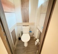 A toilet in a family house with ceramic tiles and a narrow window.