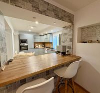 A kitchen in a family house with a bar counter and gray cabinets, flooring with a wooden decor.