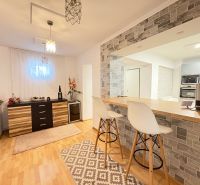 Interior of a family house with a bar counter, white chairs, and a floor with a wooden decor.