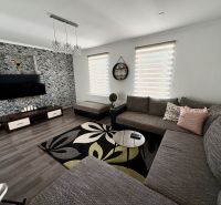 Living room in a family house with wood-patterned flooring, a large sofa, and a patterned rug.