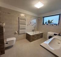 A bathroom in a family house with a bathtub, sink, and washing machine, in soft beige tones.