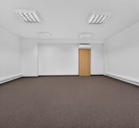 A spacious office with white walls and a brown carpet.