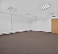 Empty office with brown carpet and white walls, the room is lit and has air conditioning.