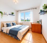 A bright bedroom with a bed, a desk, and shelves with plants in a three-room apartment.